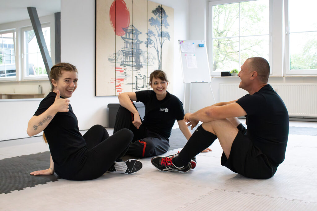 Zwei Frauen und ein Mann sitzen am Boden und unterhalten sich über das Ganzkörpertraining.