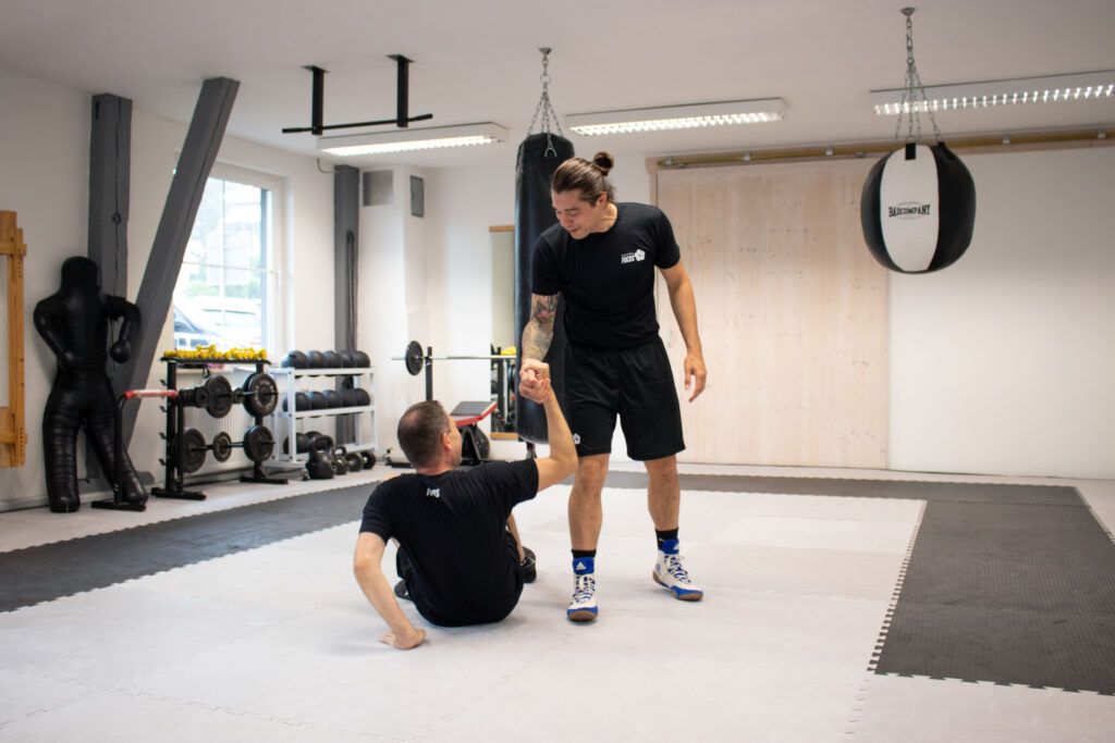 Ein Trainer der Kampfsportschule in Wangen reicht einem Schüler die Hand und hilft ihm vom Boden auf.