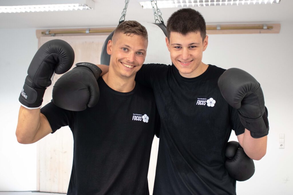 Zwei Männer tragen Boxhandschuhe und ballen ihre Fäuste, sie trainieren Boxen als Ganzkörpertraining.