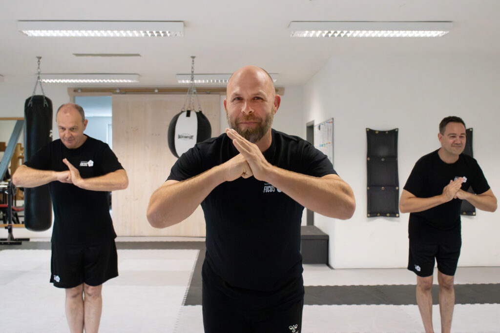 Drei Männer in Trainingskleidung die lächeln und sich leicht verbeugen.