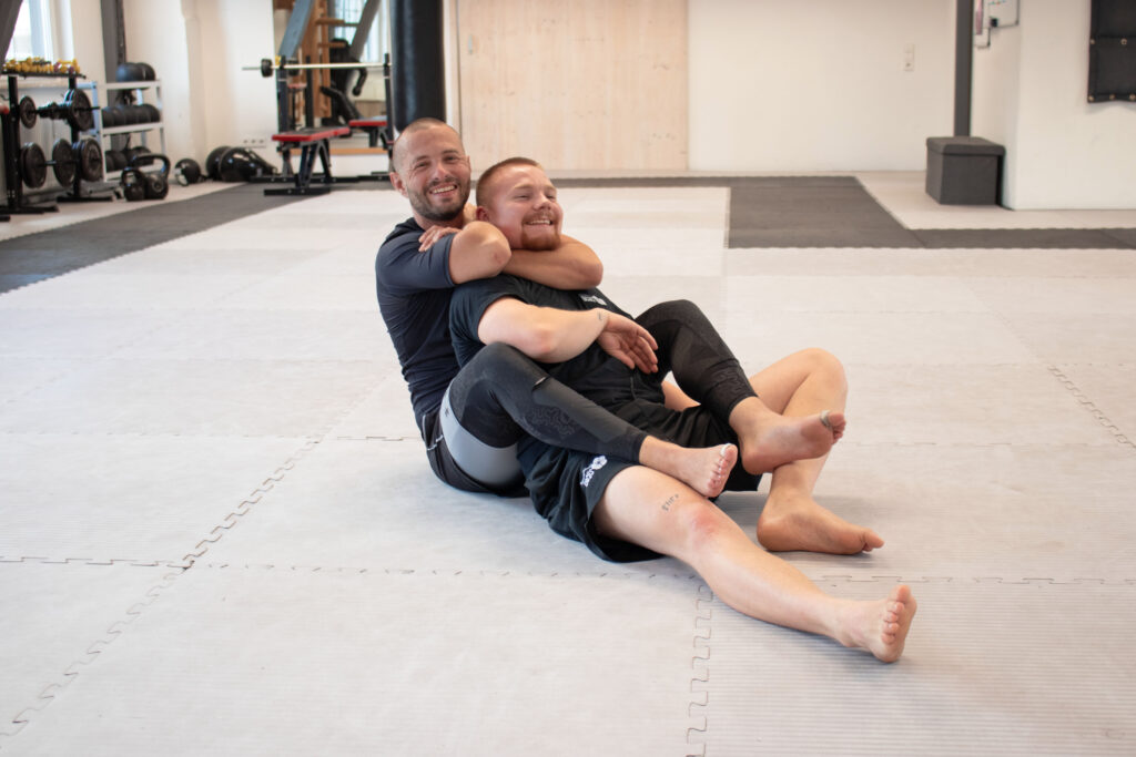 Ein Mann würgt im Grappling Training den anderen von hinten während dieser sich im versucht zu befreien.