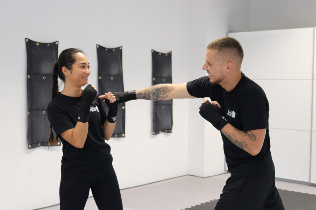 Ein Mann versucht im Kickboxtraining die Schulter einer Frau zu erreichen während die Frau ausweicht.