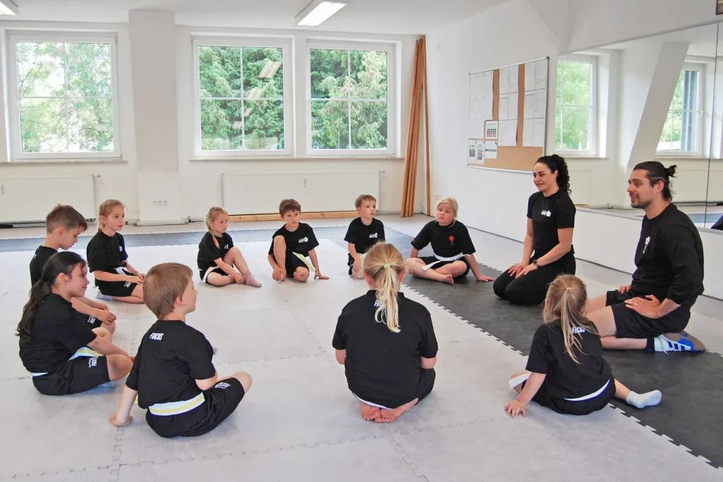 Die Kinder aus dem Selbstverteidigungskurs sitzen zusammenn mit den Trainern im Kreis und unterhalten sich.